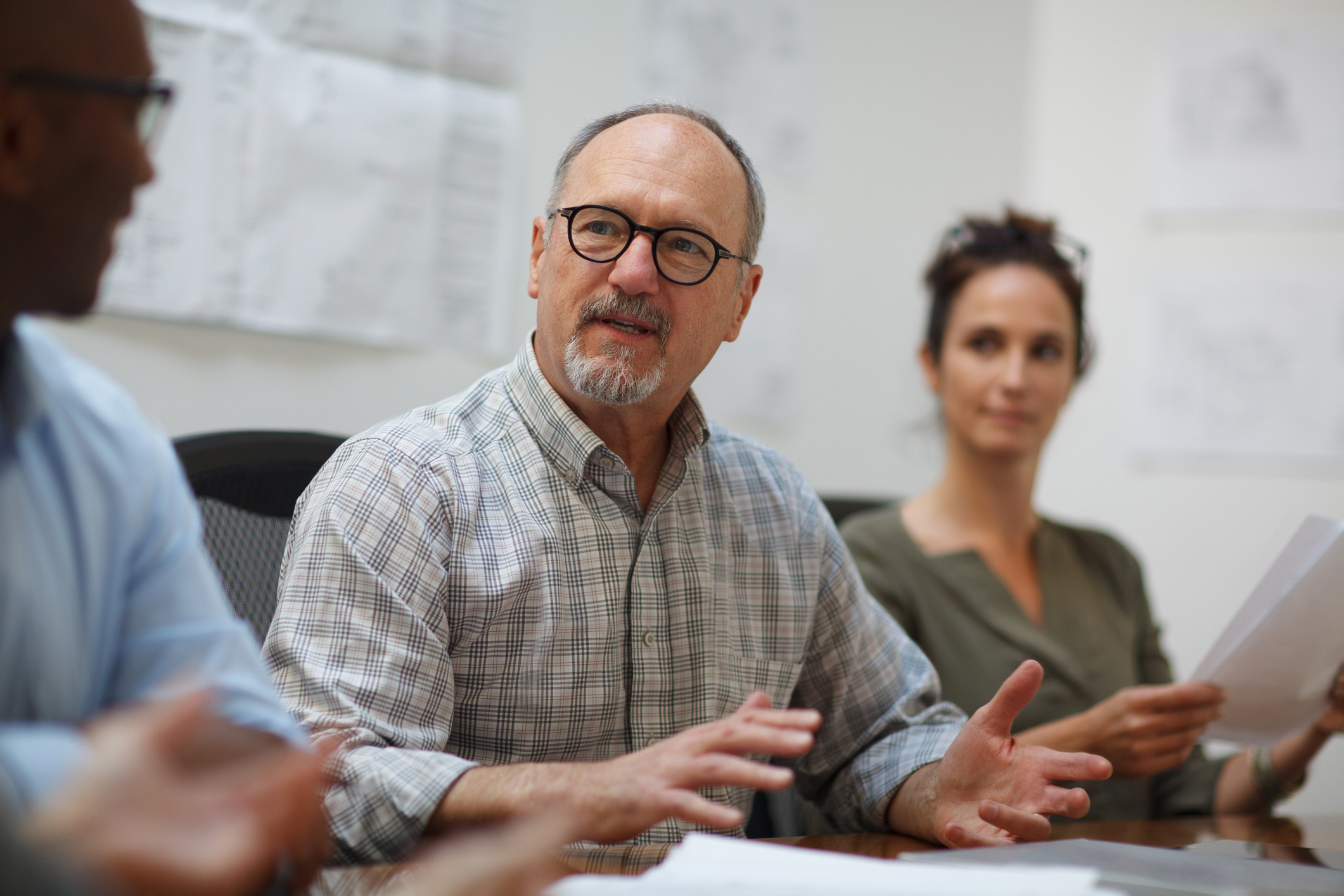 Senior man talks serious explaining in meeting with work colleagues while sitting at table in design office